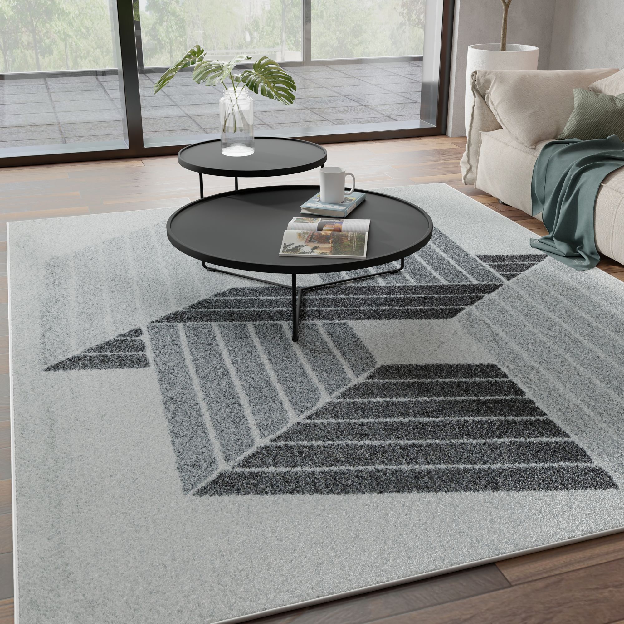 Modern living room with large windows, two black round coffee tables, and a black and gray geometric-patterned rug on a light floor.